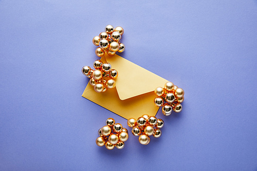 top view of shiny golden Christmas decoration and yellow envelope on blue background