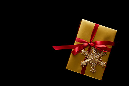 top view of shiny golden Christmas gift with red ribbon and snowflake isolated on black