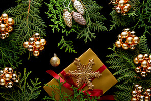 top view of shiny golden Christmas decoration, green thuja branches and gift box isolated on black