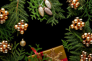 top view of shiny golden Christmas decoration, green thuja branches and gift box isolated on black with copy space
