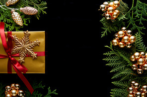 top view of shiny golden Christmas decoration, green thuja branches and gift isolated on black with copy space