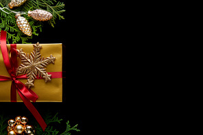 top view of shiny golden Christmas decoration, green thuja branches and gift isolated on black with copy space