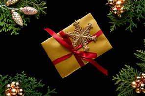 top view of shiny golden Christmas decoration, green thuja branches and gift isolated on black