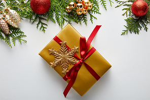top view of shiny golden and red Christmas decoration on green thuja branches, wrapped gift with snowflake isolated on white