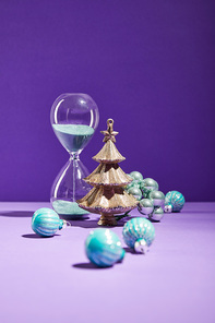 selective focus of decorative Christmas near blue baubles and hourglass on purple background