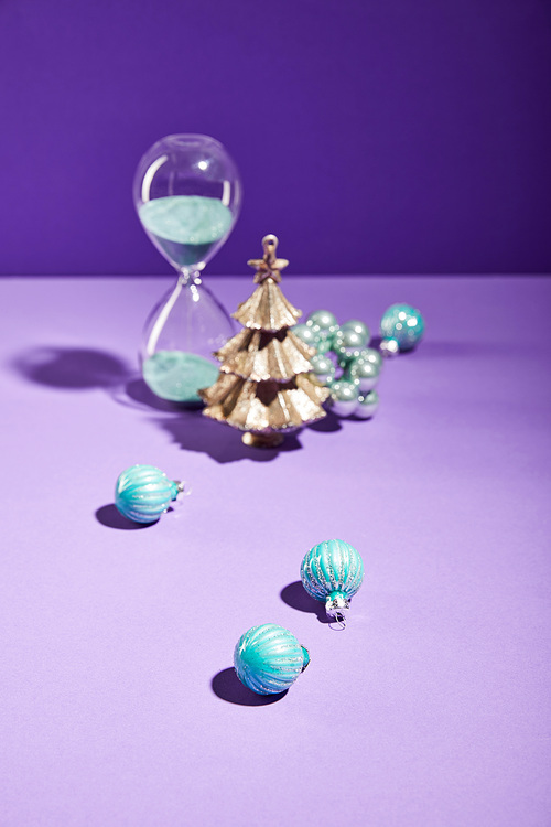 selective focus of decorative Christmas near blue baubles and hourglass on purple background