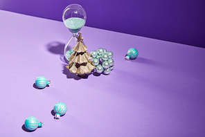 decorative Christmas near blue baubles and hourglass on purple background