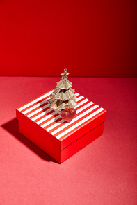striped red gift box and decorative golden Christmas tree with bauble on red background