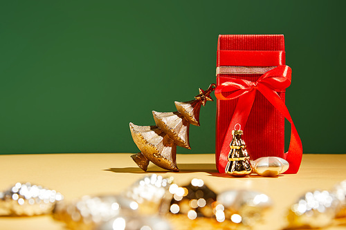 selective focus of red gift box and decorative Christmas tree with golden baubles on green background