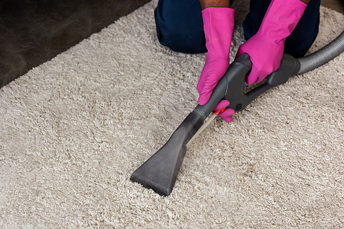 Cropped view of african american cleaner using vacuum cleaner while cleaning carpet at home