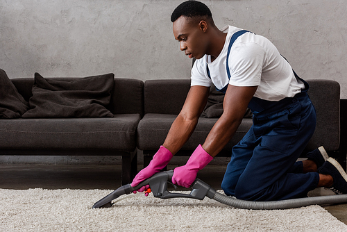 African american cleaner in rubber gloves cleaning carpet in living room