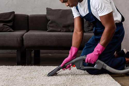 Cropped view of african american cleaner using vacuum cleaner on carpet in living room