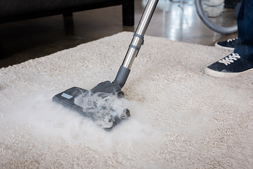 Cropped view of cleaner using vacuum cleaner with hot steam on carpet at home