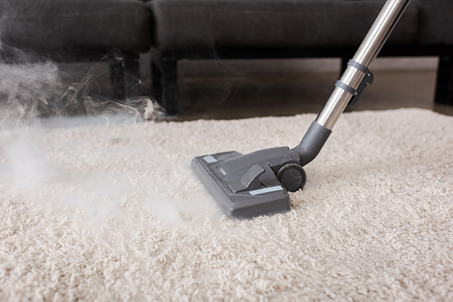 Hot steam near brush of vacuum cleaner on carpet in living room