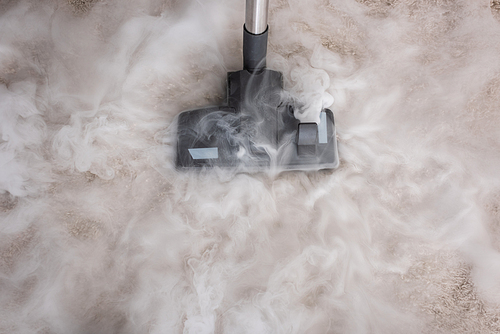 Top view of hot steam near brush of vacuum cleaner on carpet at home