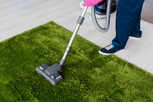 Cropped view of cleaner using vacuum cleaner on green carpet