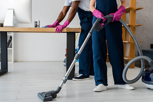 Cropped view of multiethnic cleaners using vacuum cleaner and rag in office