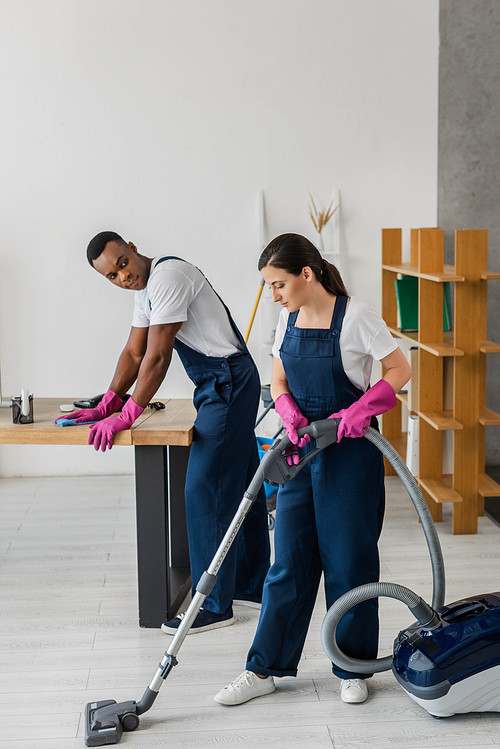 Multiethnic workers of cleaning service using rag and vacuum cleaner in office