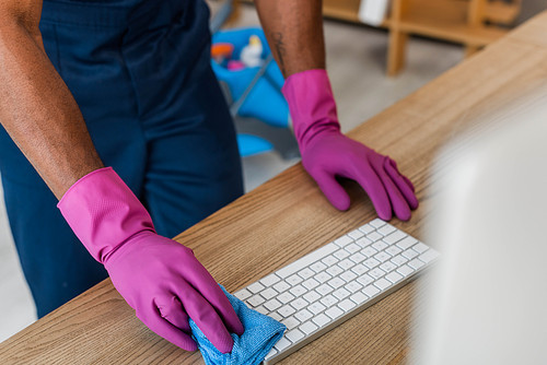 Cropped view of African american cleaner in rubber gloves cleaning computer keyboard in office