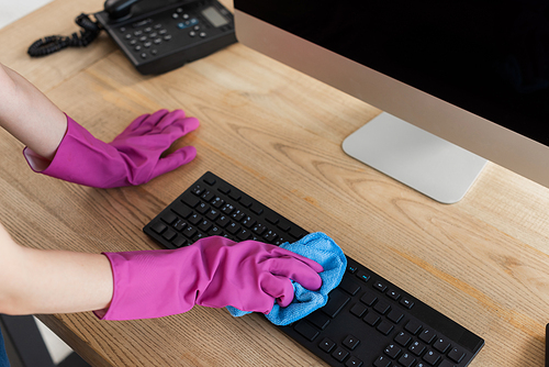 Cropped view of cleaner using rag on computer keyboard on table in office