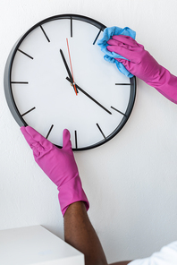 Cropped view of african american cleaner cleaning clock on wall in office