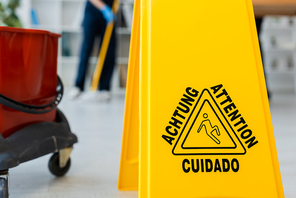 Selective focus of wet floor sign near bucket and cleaner washing floor in office