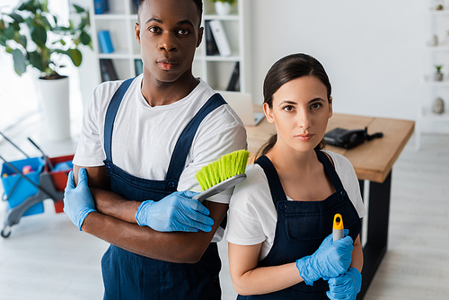 Multiethnic cleaners holding brush and mop while  in office