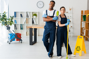 Multicultural cleaners with mop and brush  near wet floor sign in office