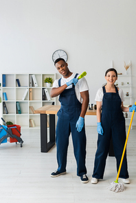 Positive multiethnic cleaners with brush and mop  in office