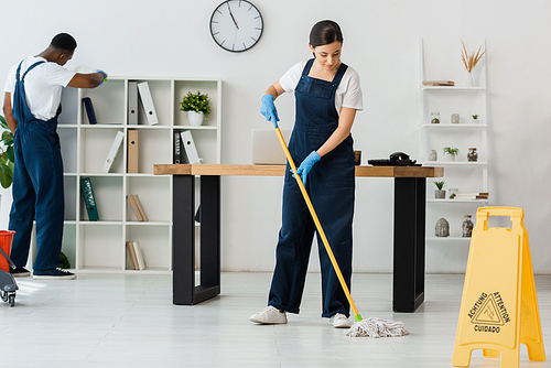 Selective focus of wet floor sign and multiethnic cleaners working in office