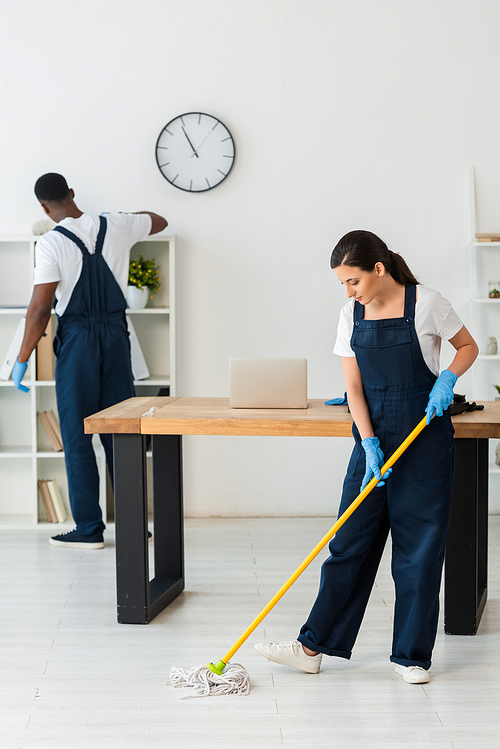 Multiethnic cleaners in uniform and rubber gloves cleaning office