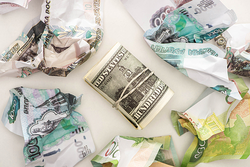 top view of cash roll with dollars near crumpled ruble banknotes isolated on white