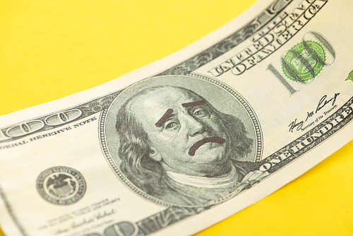 close up of dollar banknote with sad face drawing isolated on yellow