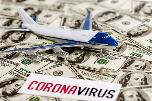 selective focus of coronavirus card and plane model on dollar banknotes, economic crisis concept