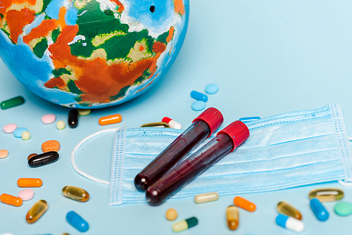 test tubes with blood samples near medical mask, pills and globe on blue background, coronavirus concept