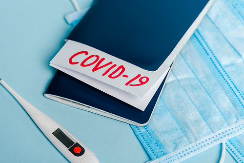 medical masks, thermometer and passports with covid-19 lettering on blue background