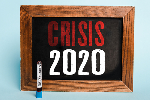 crisis 2020 lettering written on chalkboard near test tube with coronavirus blood sample on blue background