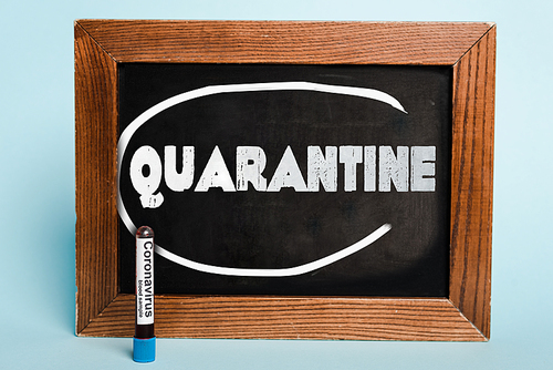 quarantine lettering written on chalkboard near test tube with coronavirus blood sample on blue background