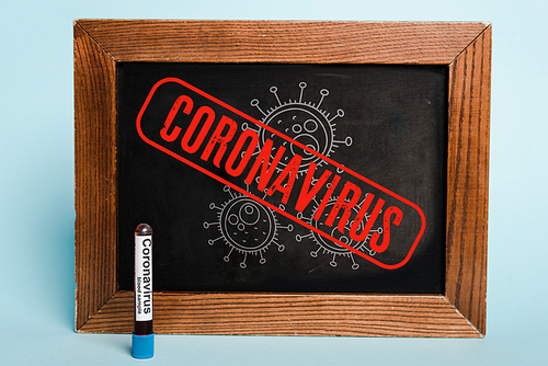 coronavirus lettering written on chalkboard near test tube with blood sample on blue background