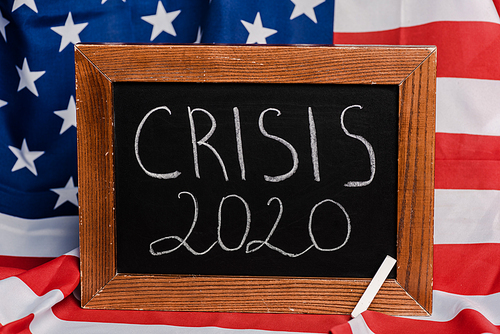 crisis 2020 lettering written on chalkboard on american flag background, coronavirus concept