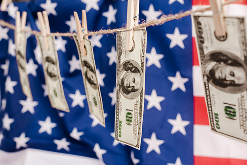 selective focus of dollar banknotes hanging on rope on american flag background, coronavirus concept