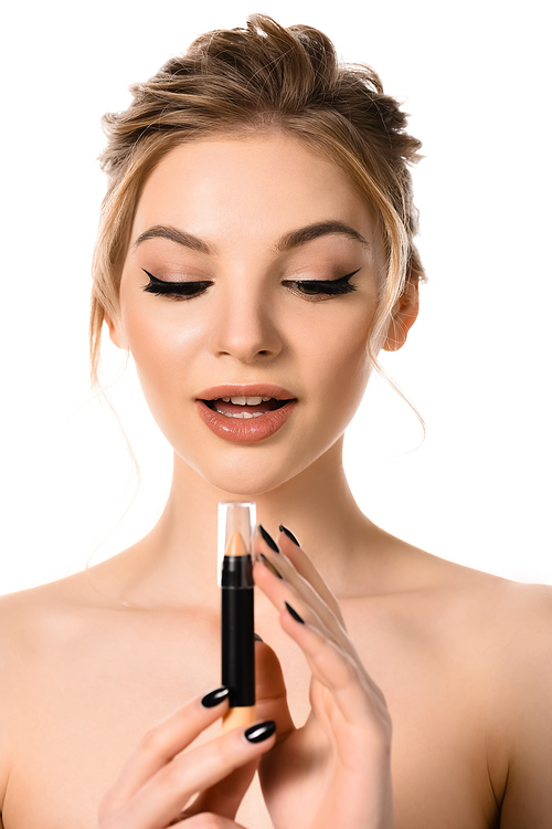 naked beautiful blonde woman with makeup and black nails looking at stick concealer isolated on white