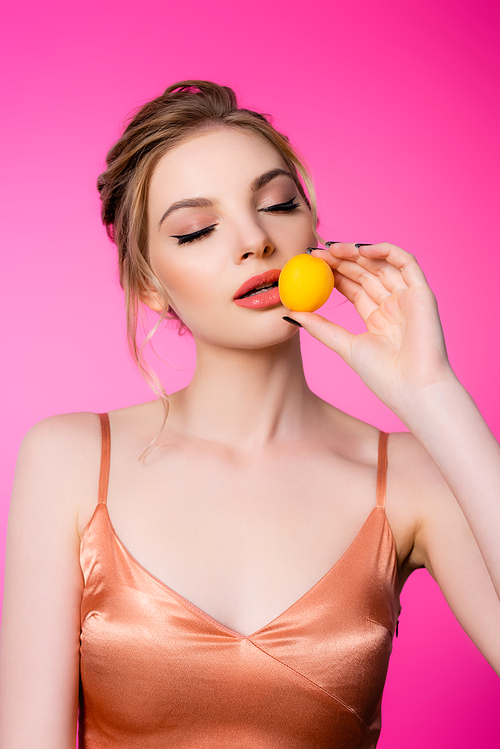 elegant beautiful blonde woman with closed eyes in silk dress holding apricot isolated on pink