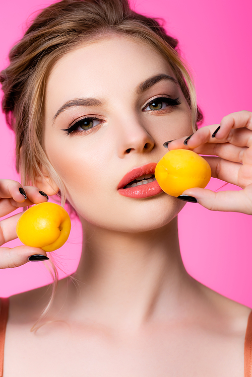 elegant beautiful blonde woman holding apricots isolated on pink