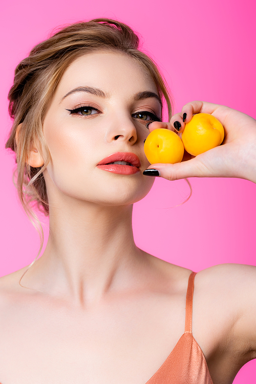 elegant beautiful blonde woman holding apricots isolated on pink