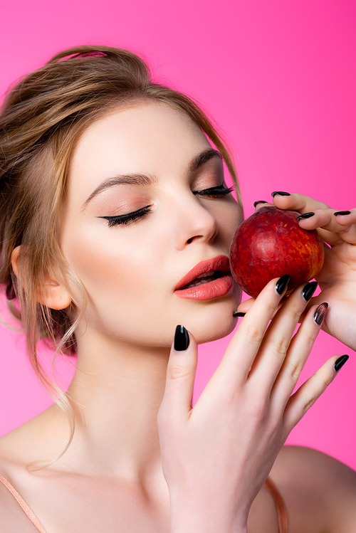 elegant beautiful blonde woman with closed eyes holding peach isolated on pink