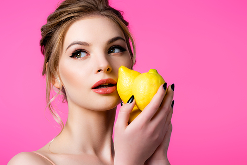 beautiful blonde woman holding ripe lemons isolated on pink