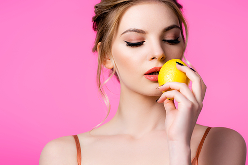 elegant beautiful blonde woman holding ripe lemon near lips isolated on pink