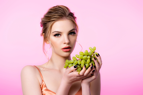 elegant beautiful blonde woman holding green grapes isolated on pink