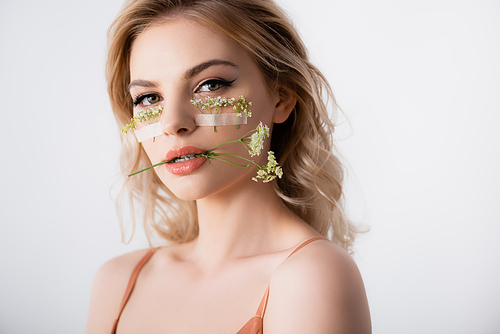 beautiful blonde woman in silk dress with wildflowers under eyes and in mouth isolated on white